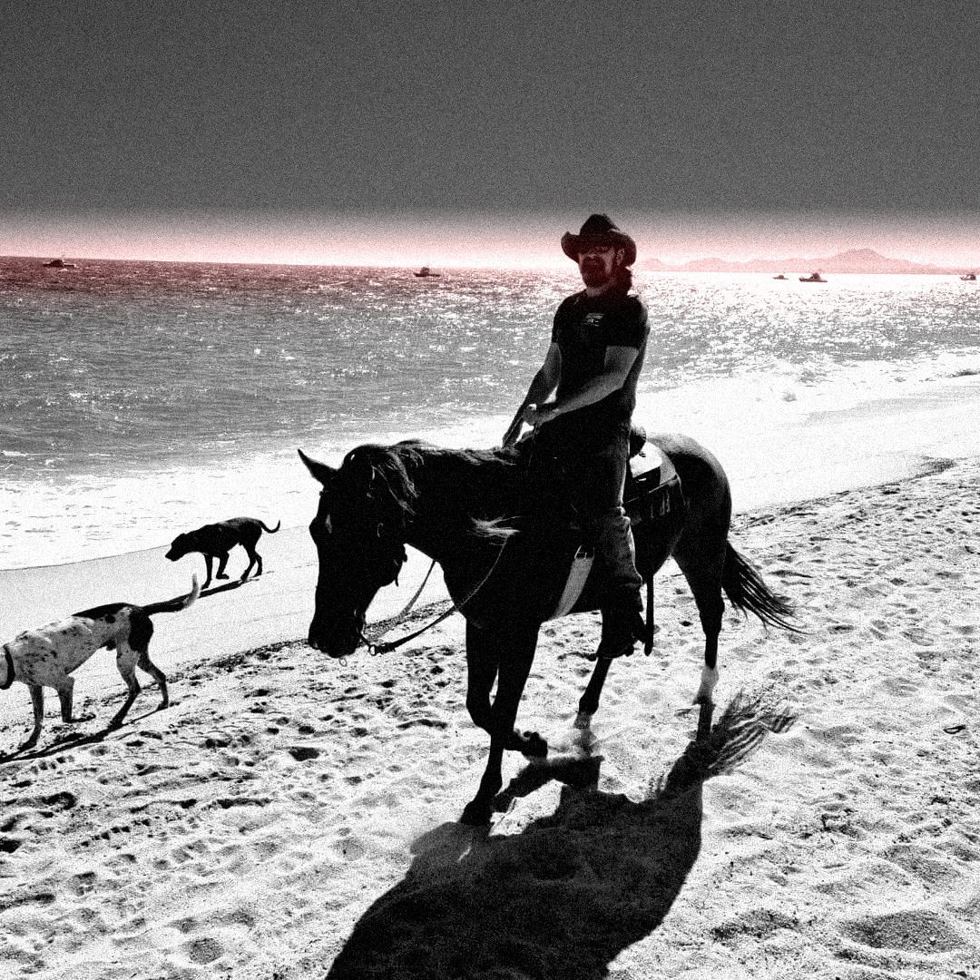 Jeff McKinney, Fort Worth REALTOR, riding a horse on the beach in a black cowboy hat